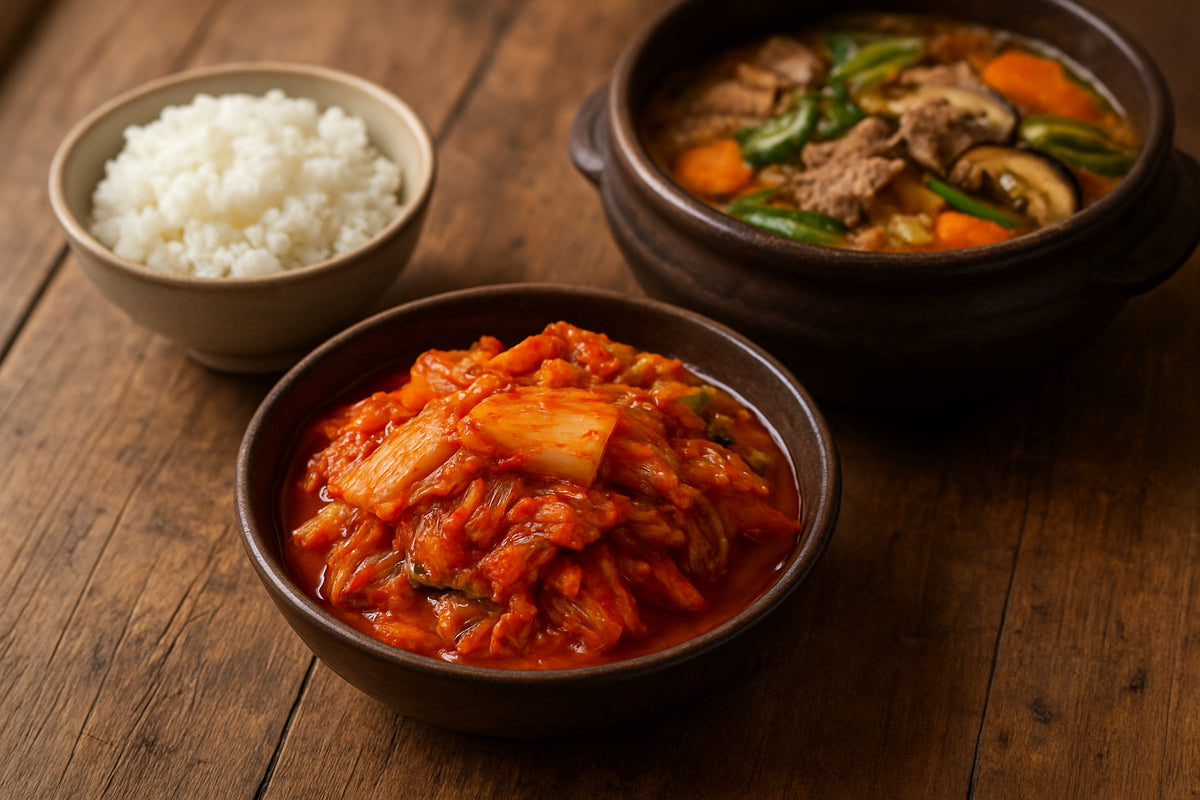 Frisch zubereitetes Kimchi in einer Schale auf einem Holztisch neben koreanischem Hot Pot und Reis in einer authentischen koreanischen Kü...